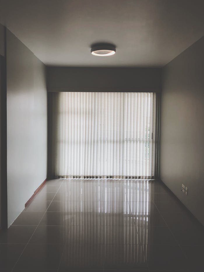 Spacious empty room with modern design featuring large window blinds and tiled floor.